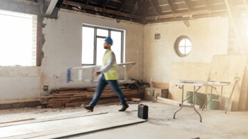Artisan en gilet jaune marchant dans un chantier de rénovation intérieure