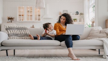 Femme sur son ordinateur portable avec son enfant jouant avec un smartphone près d'elle